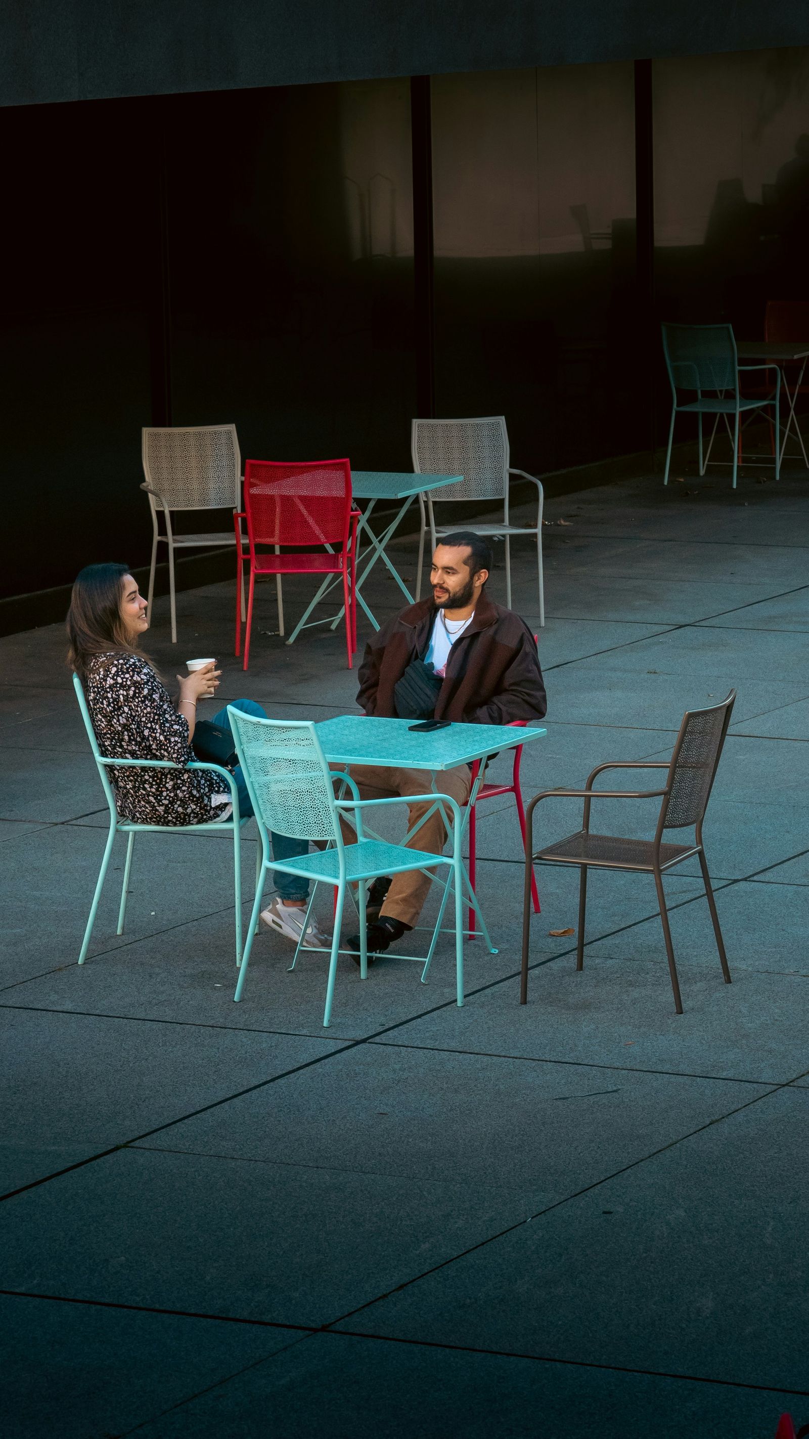 Two people talking at an outdoor table on a concrete patio