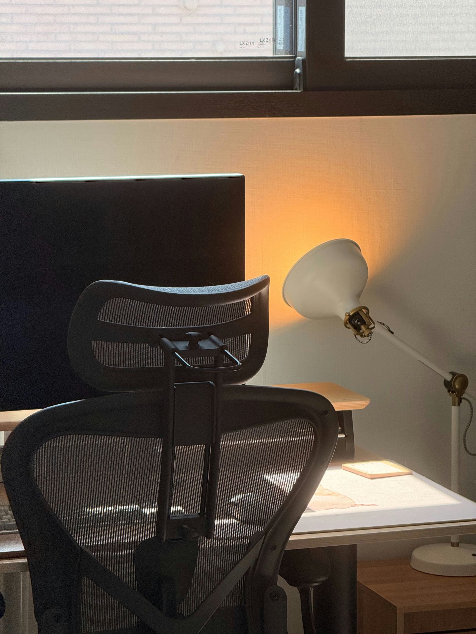 A lit desk lamp beside a monitor and an office chair